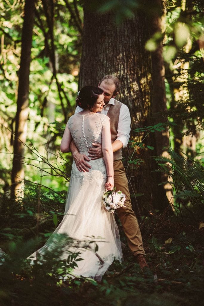 groom hugs his bride in forest