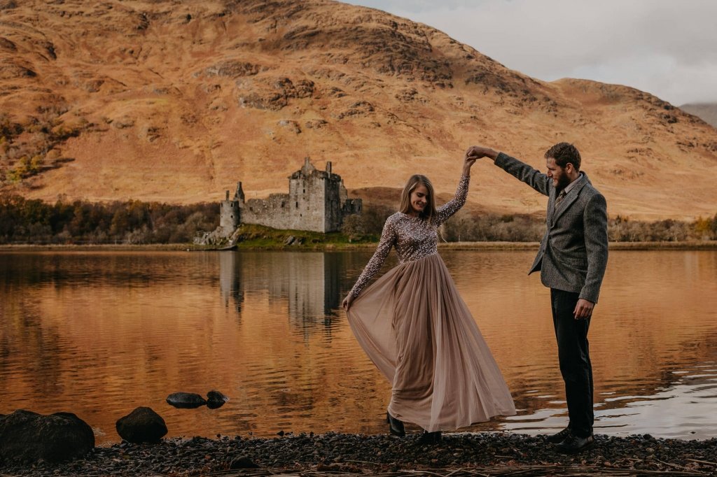 scottish highlands engagement location where bride and groom dance with a castle behind them.